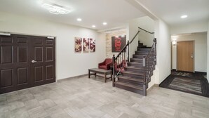 A spacious foyer with a wooden staircase, a bench, and a door leading to a room. - Red Roof Inn & Suites Carrollton, Ga-west Georgia (Carrollton)