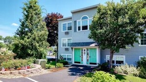 A two-story building with a green door and windows, surrounded by trees and a landscaped garden.