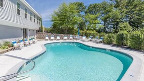 A swimming pool with lounge chairs, a stone wall, and a building with windows.