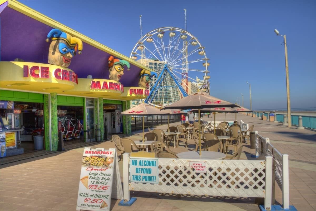 A boardwalk with an ice cream shop and a Ferris wheel in the background.