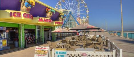 A boardwalk with an ice cream shop and a Ferris wheel in the background.