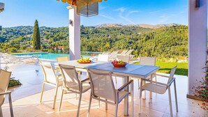 Une terrasse avec une table et des chaises, donnant sur une piscine et un paysage montagneux.