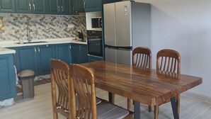 Una cocina con armarios color turquesa, un refrigerador de acero inoxidable, un microondas y una mesa de comedor de madera con cuatro sillas.