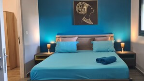 Un dormitorio con una cama, dos mesitas de noche, una lámpara de noche, una obra de arte en la pared y una ventana.