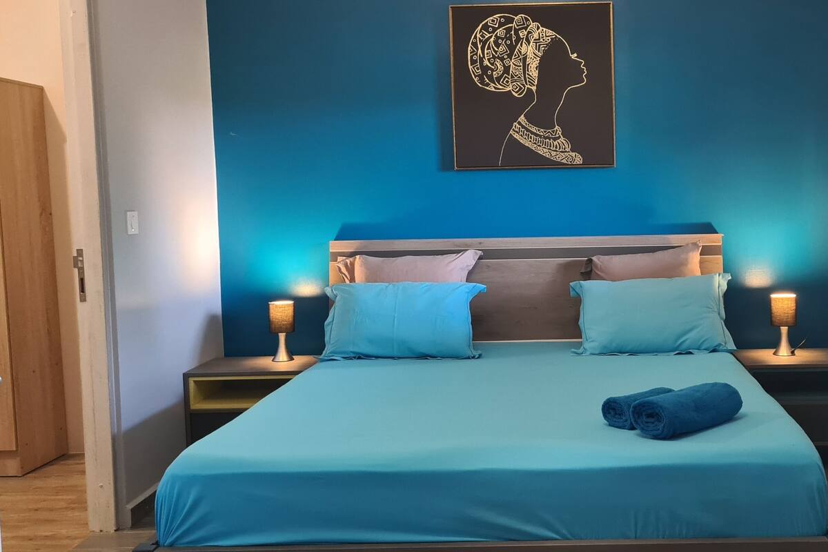 A bedroom with a bed, two bedside tables, a nightstand, a wall-mounted artwork, and a window.
