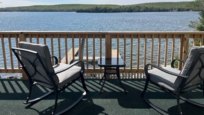 A deck with two rocking chairs and a small table, overlooking a lake with a forested shoreline. - Deepwater Lodge Chicagon Lake- Sleeps 24-Pontoon included-DM for June specials! (Crystal Falls)