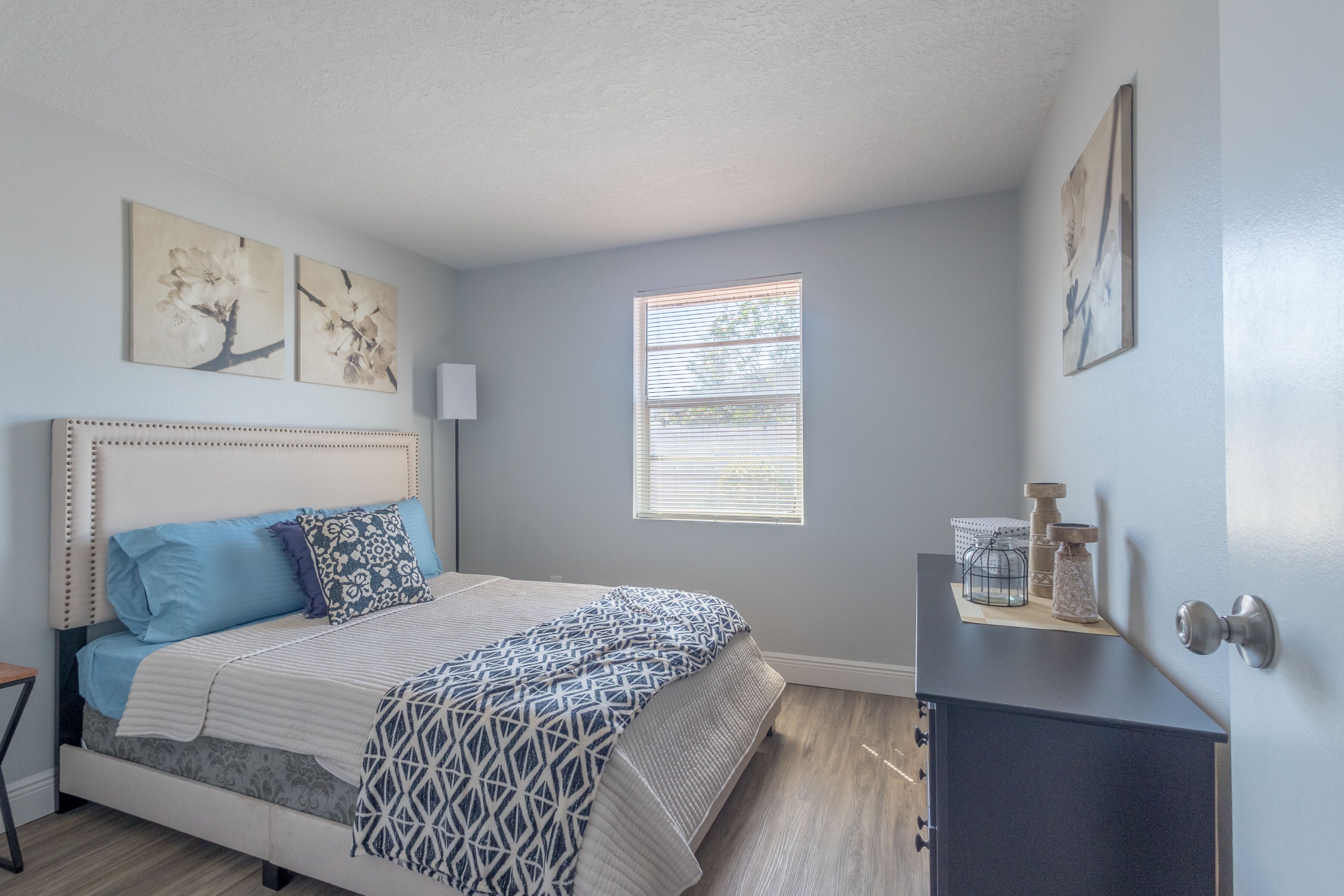 A bedroom with a bed, a nightstand, a window, and wall art.