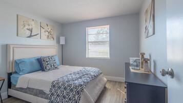 A bedroom with a bed, a nightstand, a window, and wall art.