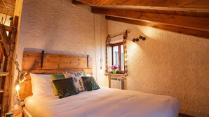 A cozy bedroom with a wooden headboard, a large bed with multiple pillows, a window with curtains, and a wall-mounted mirror. - The mountain loft with the most beautiful park on Lake Maggiore as its garden (TRAREGO VIGGIONA)