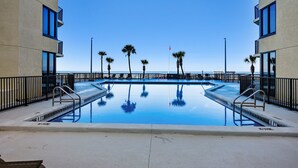 A swimming pool with clear blue water, surrounded by palm trees and modern buildings.