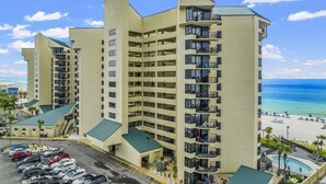A multi-story hotel with balconies, a parking lot, and a pool area.