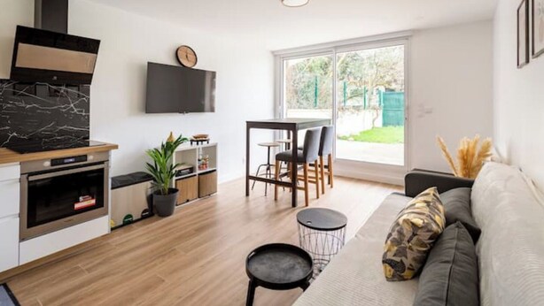A modern kitchen with a built-in oven, a dining area with a table and chairs, a sofa, and a large window offering a view of the outdoors. - Amazing flat, Paris suburb, near Versailles ,Orly (Orsay)