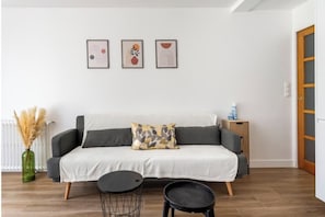 Una sala de estar moderna con un sofá, una mesa de centro y una mesita auxiliar. Hay tres obras de arte enmarcadas en la pared.