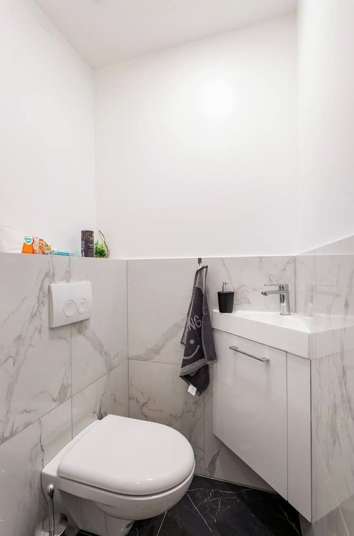 Un baño moderno con inodoro blanco, paredes de mármol, suelo negro, un lavabo con grifo y una toalla colgada en la pared.