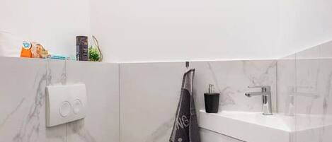 Un baño moderno con inodoro blanco, paredes de mármol, suelo negro, un lavabo con grifo y una toalla colgada en la pared.