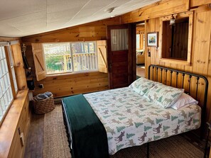 Une pièce de cabane en bois comprenant un lit, une fenêtre, une porte et un petit panier.