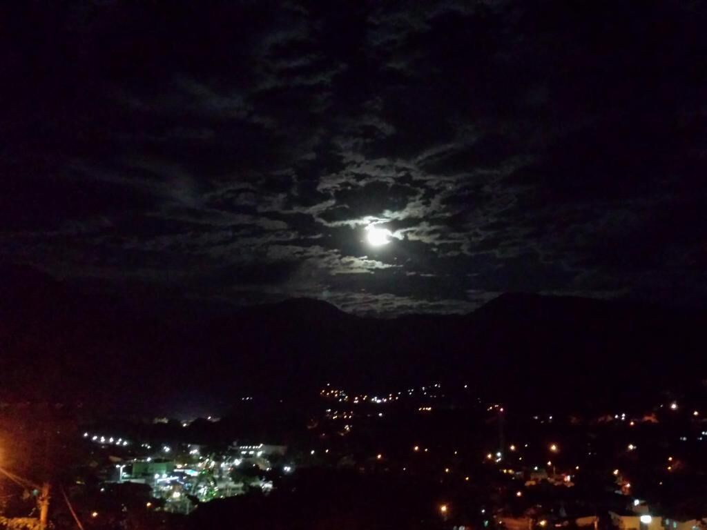 Ein Nachtblick auf eine Stadt mit sichtbarem Mond und vereinzelten Wolken.