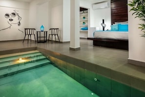 A modern hotel room with a glass-bottomed pool, a bed with blue bedding, and a minimalist decor.