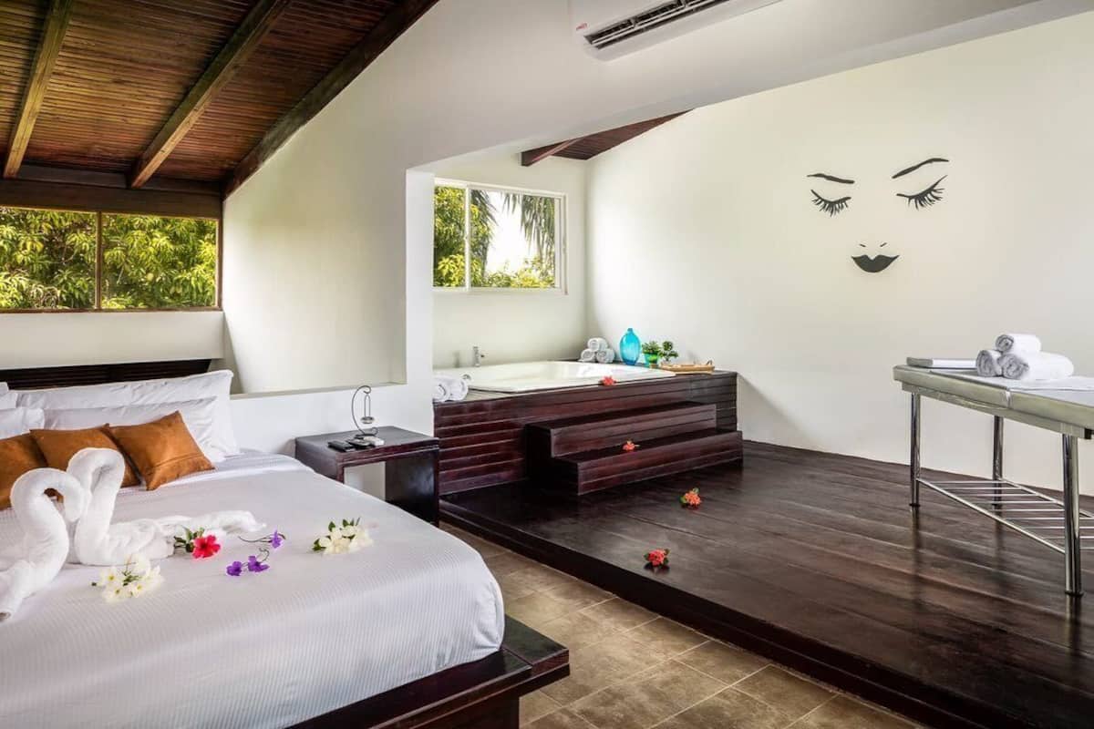 Une chambre d’hôtel avec un lit, une salle de bain dotée d’un grand miroir et une vue sur la verdure environnante.