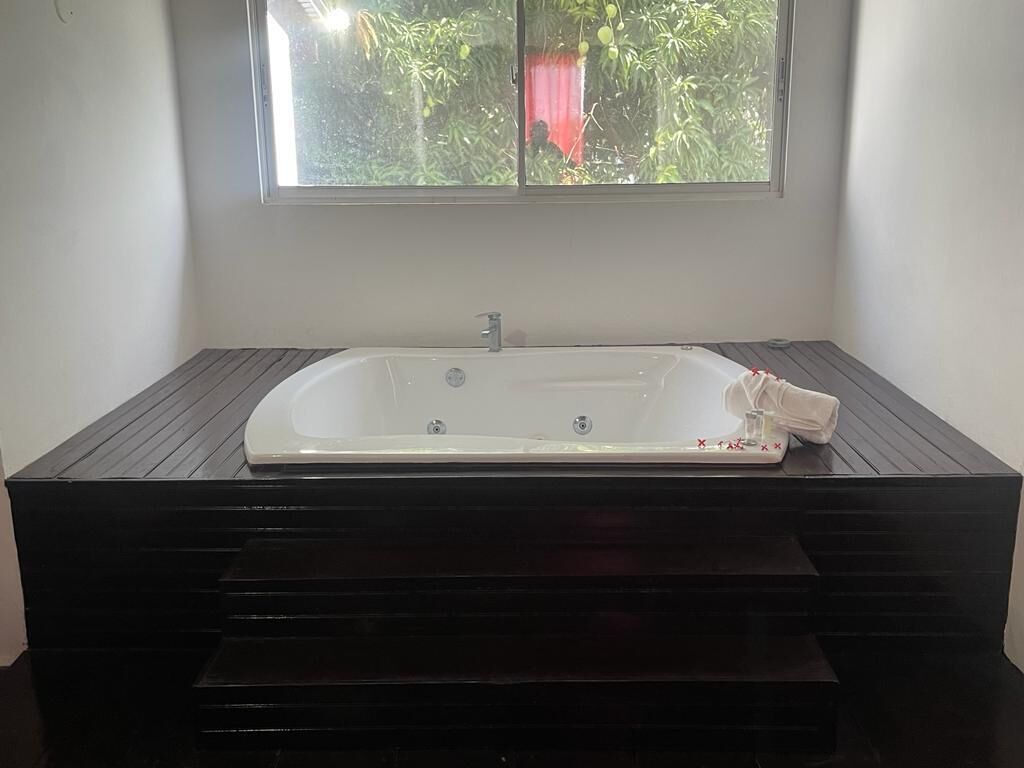 Una bañera rectangular sobre una plataforma de madera oscura, con una ventana encima.