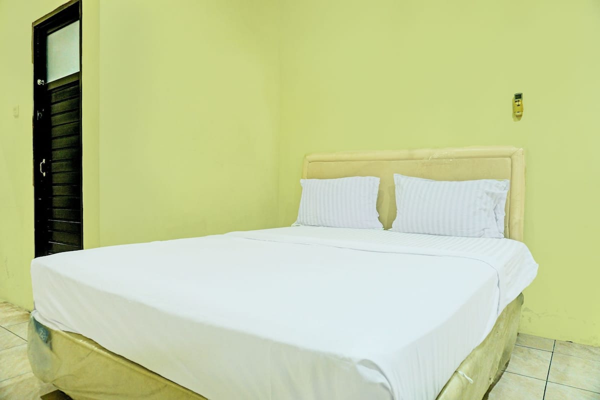 Un lit avec du linge de lit blanc, une tête de lit beige et un mur sobre.