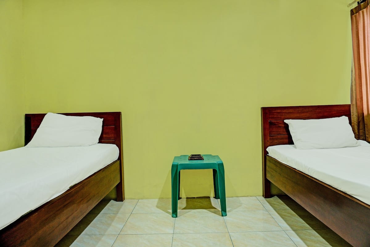 Une pièce avec deux lits en bois, chacun recouvert de draps blancs, et un petit tabouret vert placé au centre.