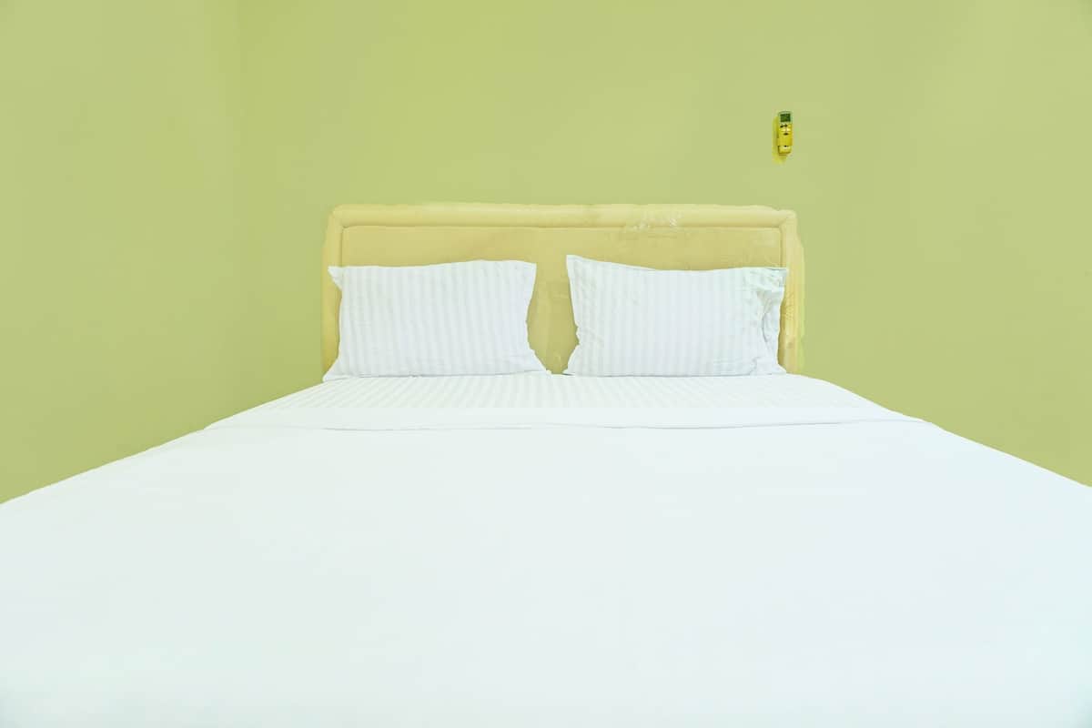 Un lit avec une literie blanche et une tête de lit jaune, dans une pièce aux murs vert clair.