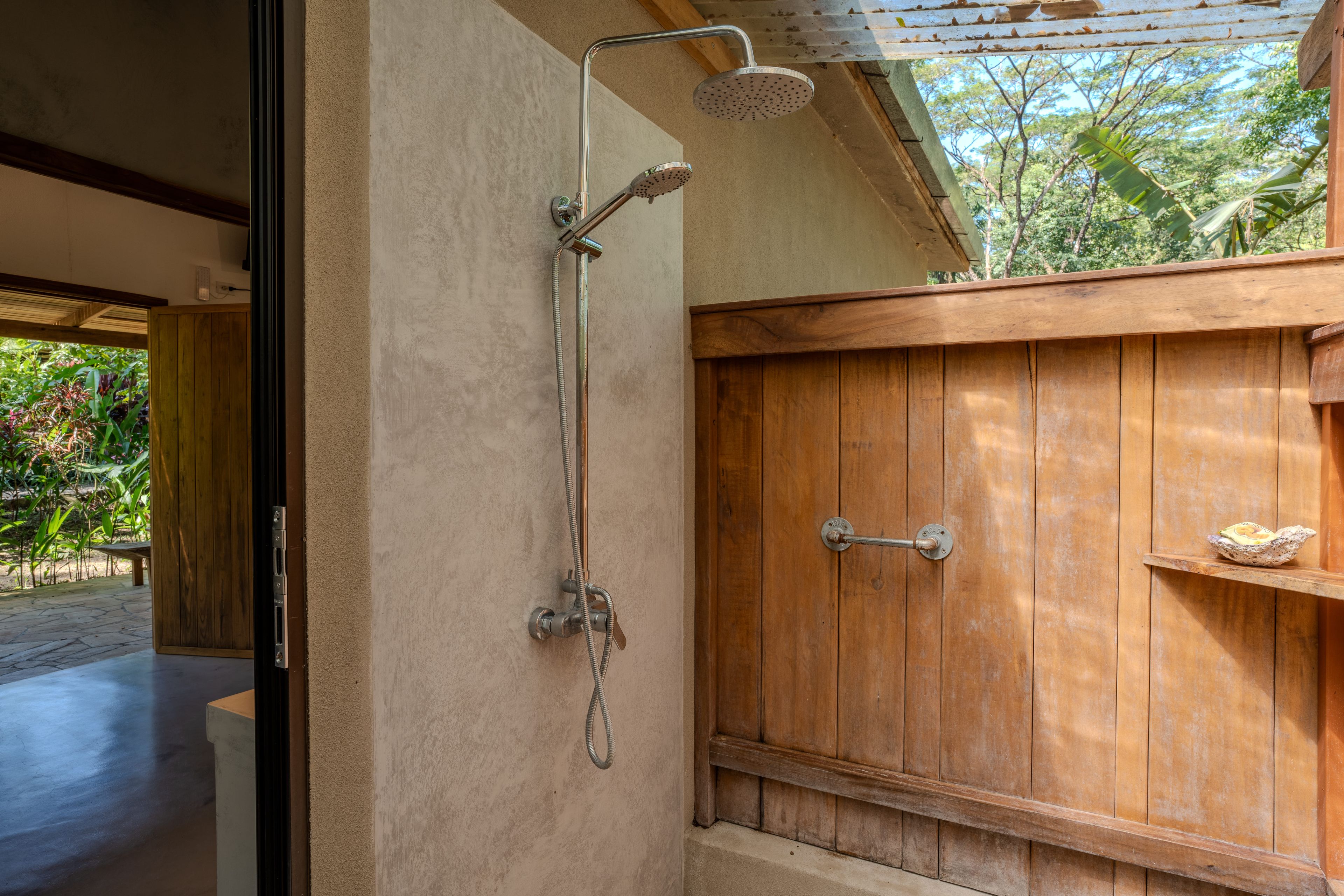 Eine Dusche mit Regendusche und Handbrause, ein Holzschrank mit Ablagefläche und Blick ins Freie.