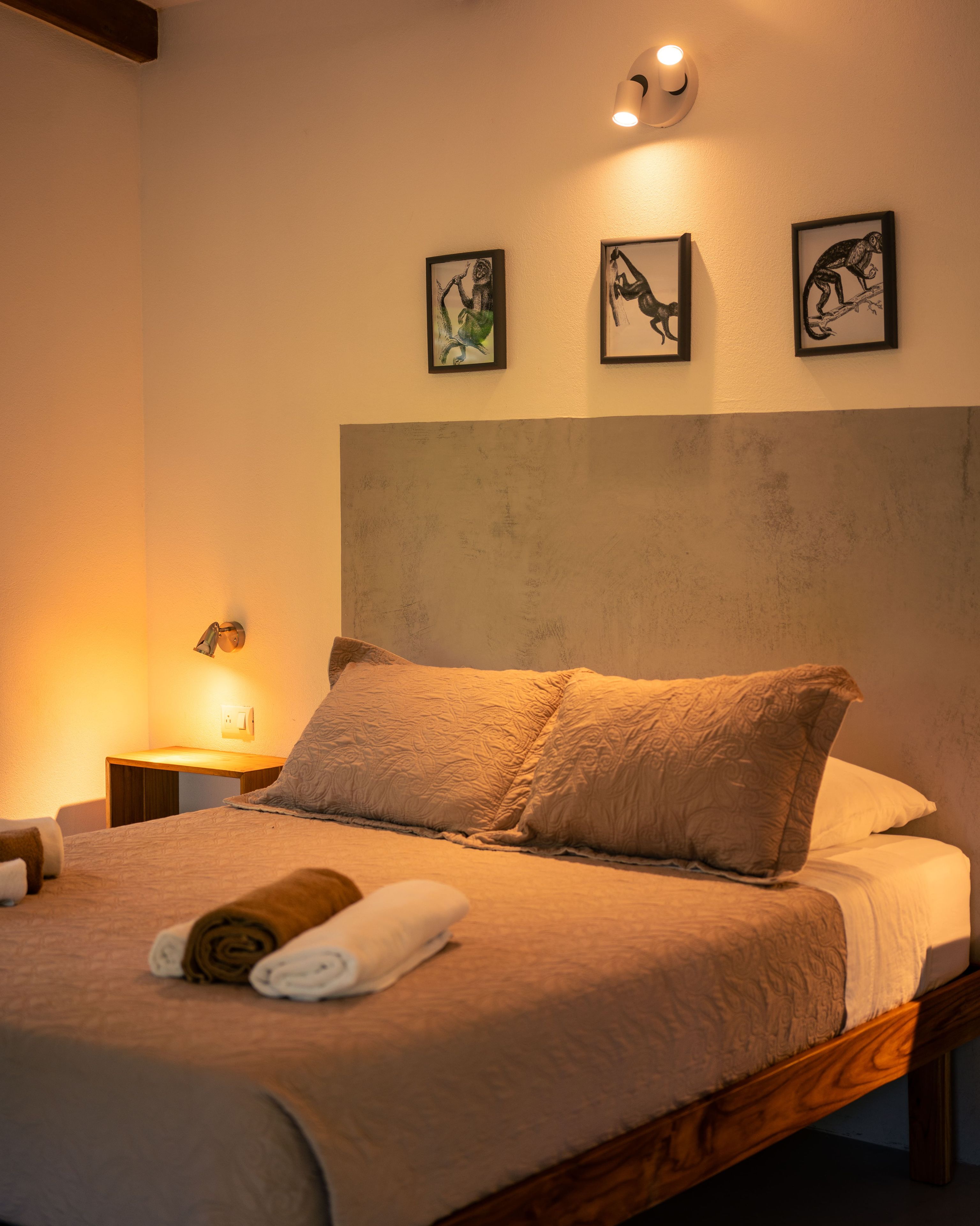 A neatly made bed with a headboard, a bedside lamp, and three framed pictures on the wall.