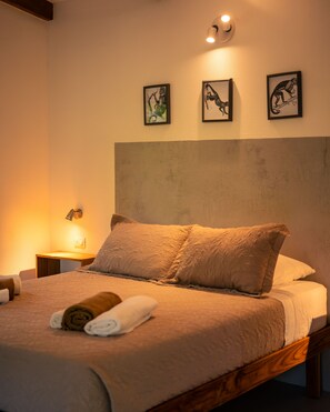 A neatly made bed with a headboard, a bedside lamp, and three framed pictures on the wall.