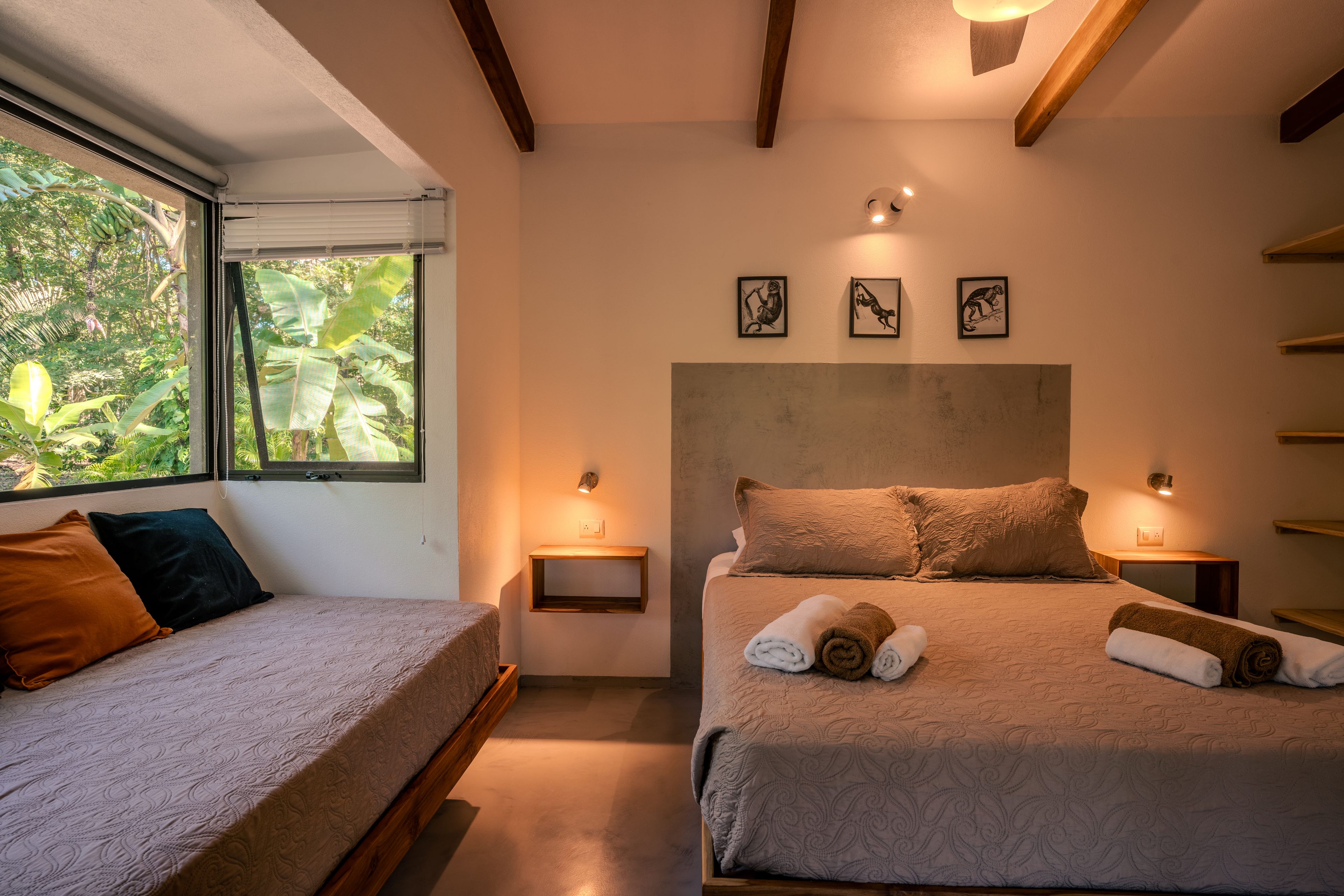 Un dormitorio con una cama, una cama individual, una ventana con vistas a zonas verdes y obras de arte colgadas en la pared.