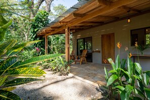 A covered outdoor seating area with a wooden pergola, a stone patio, and lush tropical plants.
