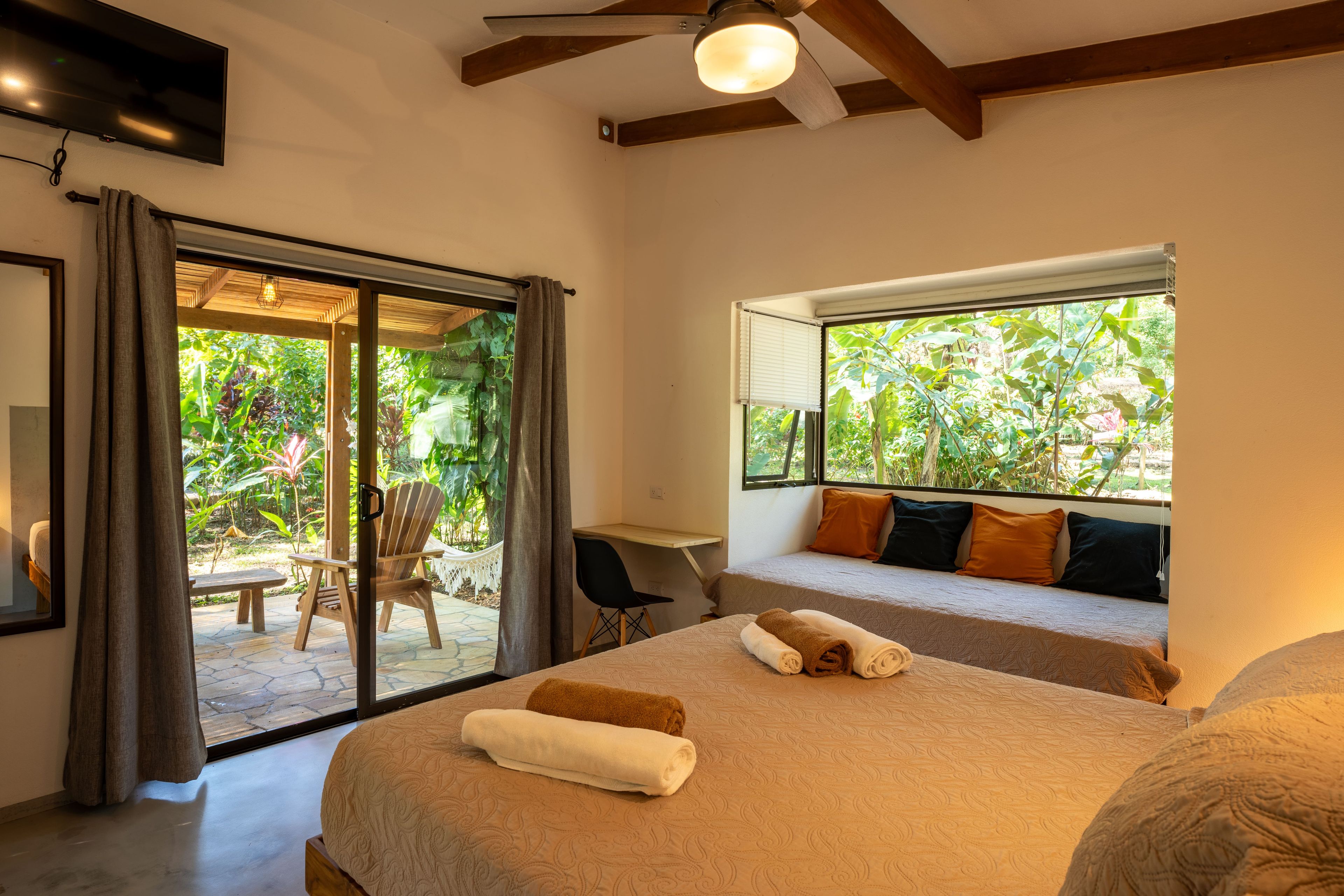 A bedroom with a bed, a desk, and a view of greenery outside.