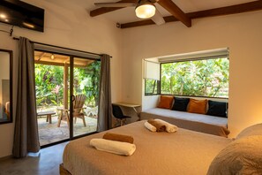 A bedroom with a bed, a desk, and a view of greenery outside.