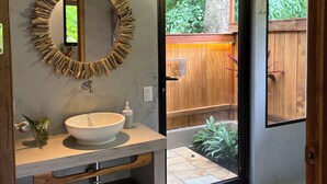 A modern bathroom with a large round mirror, a white sink, and wooden shelves.