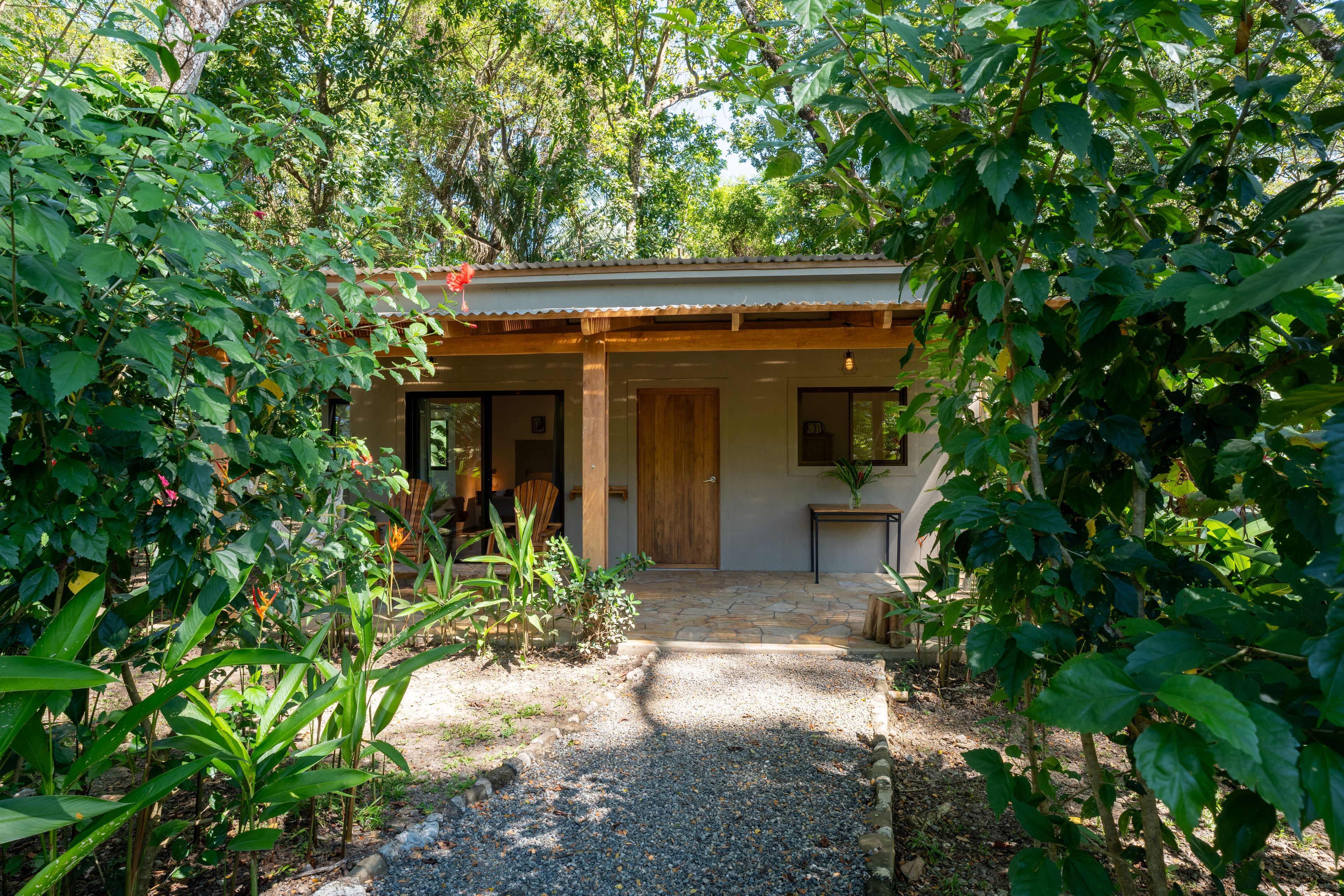 A house with a covered porch, a gravel path leading to the entrance, and lush greenery surrounding the property.