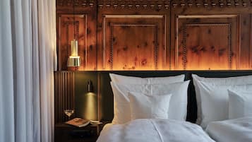 Een hotelkamer met een houten hoofdeinde, twee bedden, een nachtkastje met een lamp, een boek en een glas wijn.