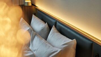 Habitación de hotel con cabecera oscura, almohadas blancas y una lámpara fijada a la pared.