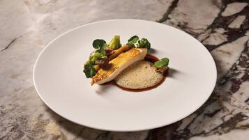 Un plato blanco con un trozo de pescado, verduras y una salsa sobre una superficie de mármol.