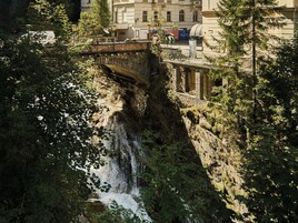 A stone bridge over a waterfall with a building in the background.