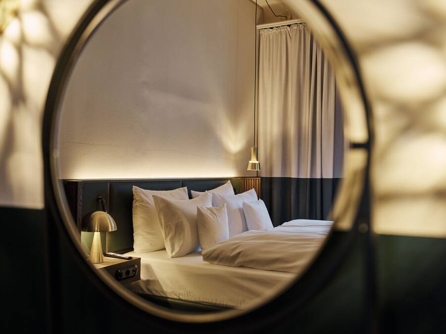 Vista circular de una habitación de hotel con cama, almohadas, lámpara de noche y cortina.