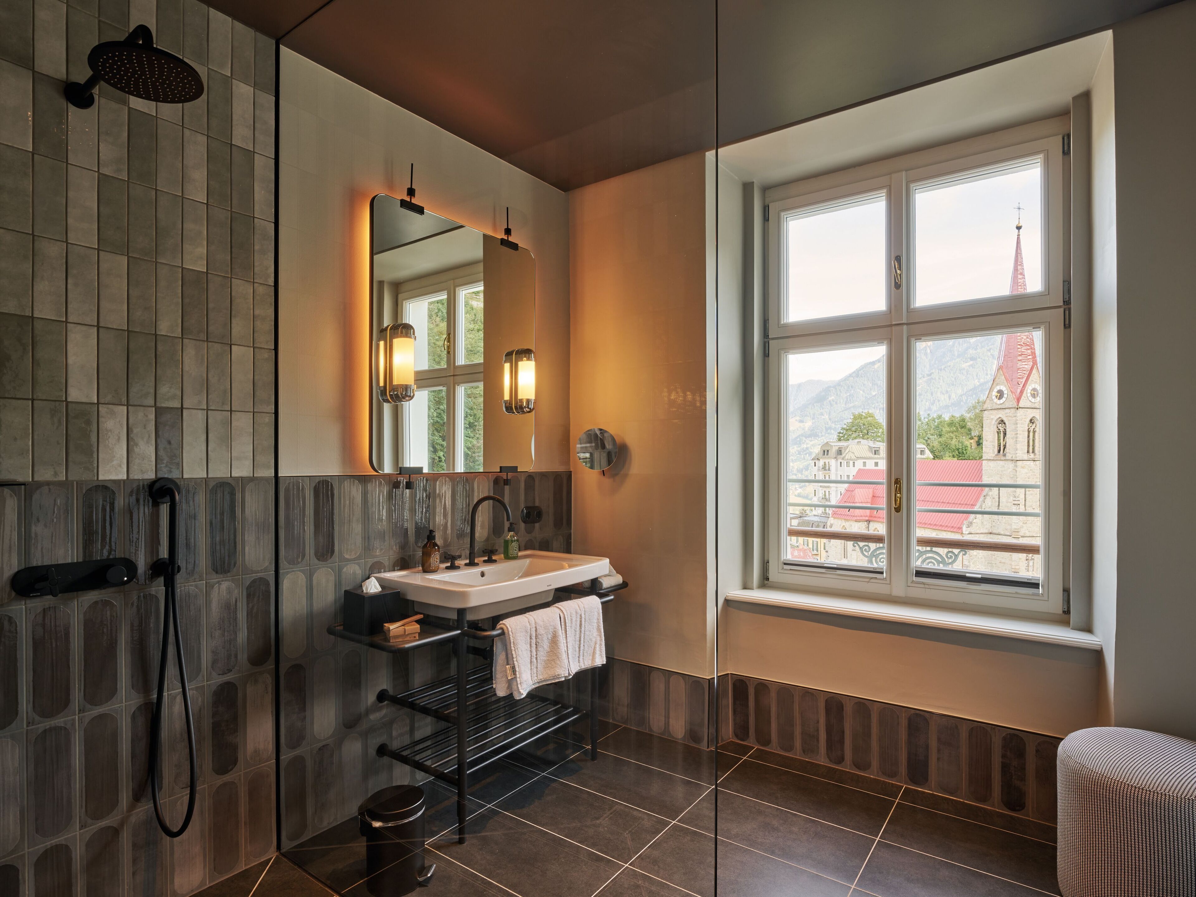 Ein modernes Badezimmer mit einem großen Spiegel, einer Dusche und einem Fenster mit Blick auf ein Gebäude.