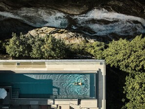 A swimming pool with a person swimming, surrounded by trees and a rocky cliff. - A-ROSA Straubinger Grand Hotel Bad Gastein - Adults Only (Bad Gastein)