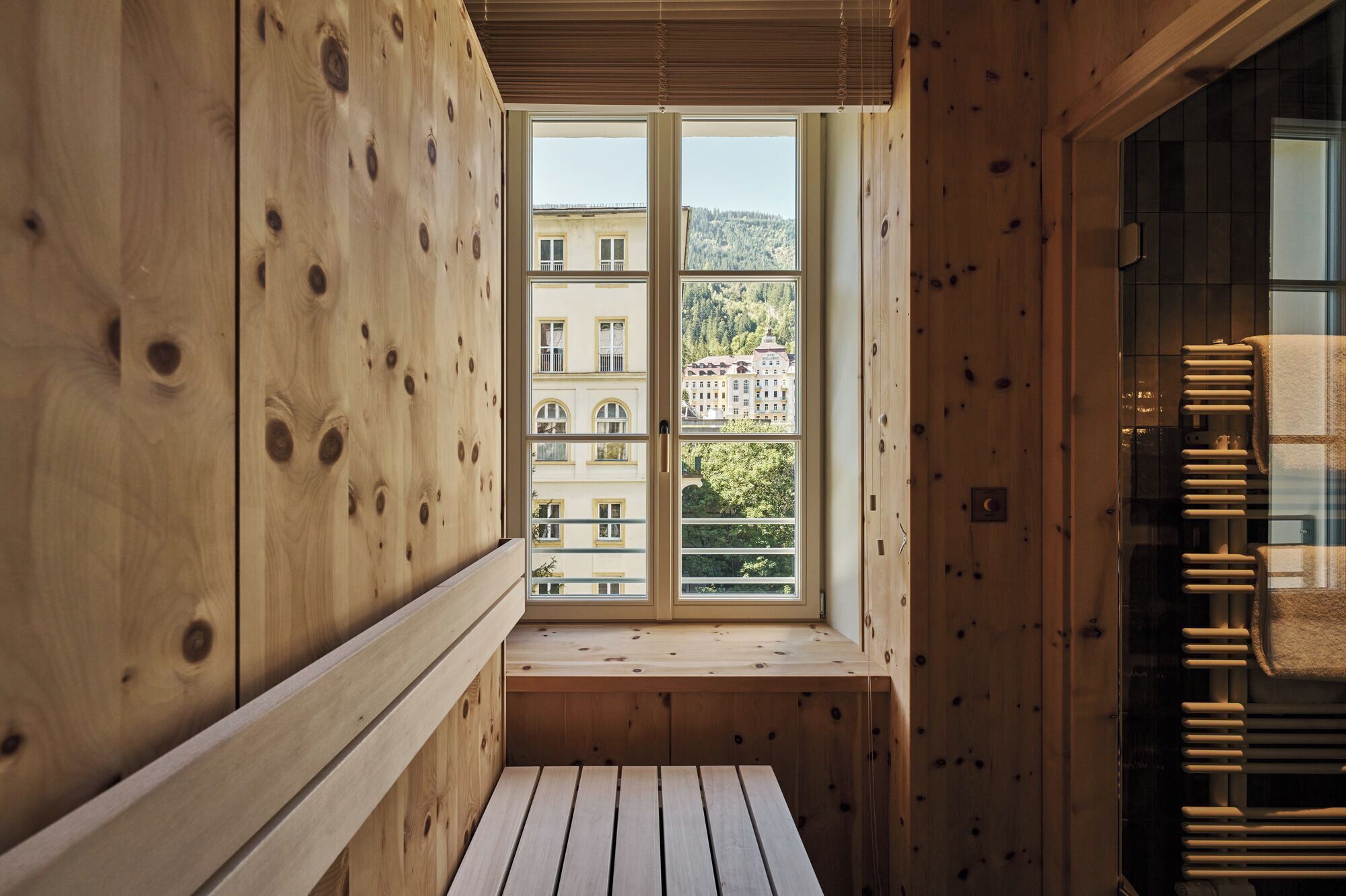 A wooden cabin with a window overlooking a building and trees.
