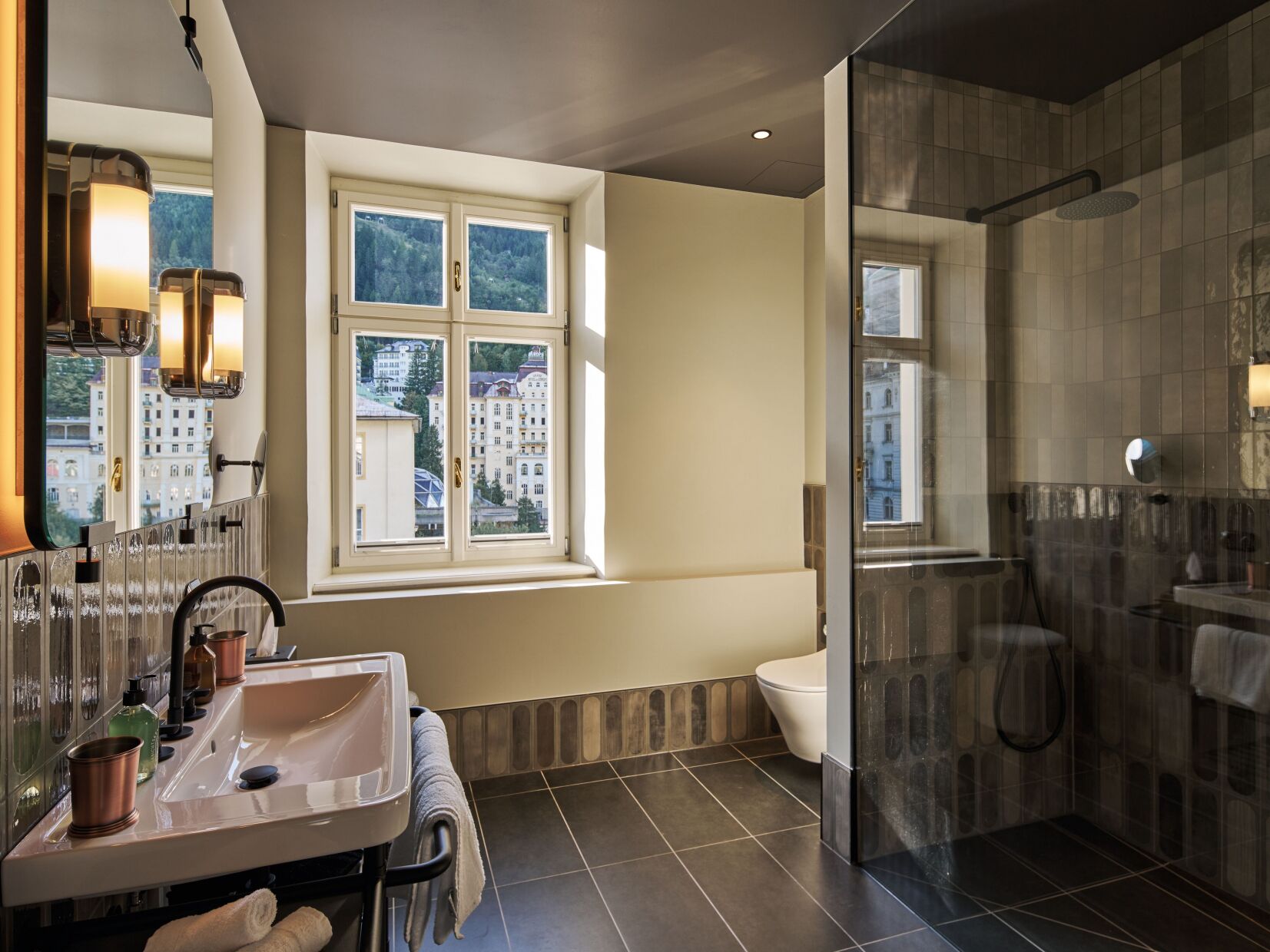A modern bathroom with a large window, a glass shower enclosure, and a sink with toiletries.
