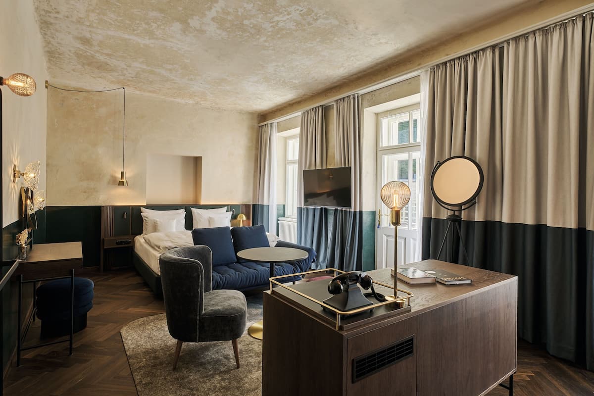 A modern hotel room with a bed, a sofa, a desk, and a TV.