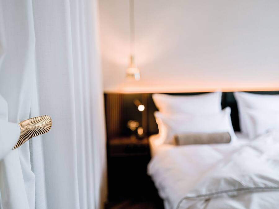 A hotel room with a bed, a bedside table, and a lamp.