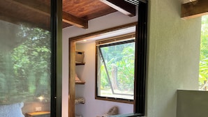 A wooden table with a vase of flowers, a window with a view of greenery, and a shelf with baskets. - Feeling Trees Jungle Lodge-Casa Caracoles walking distance to the beach (Cabuya)