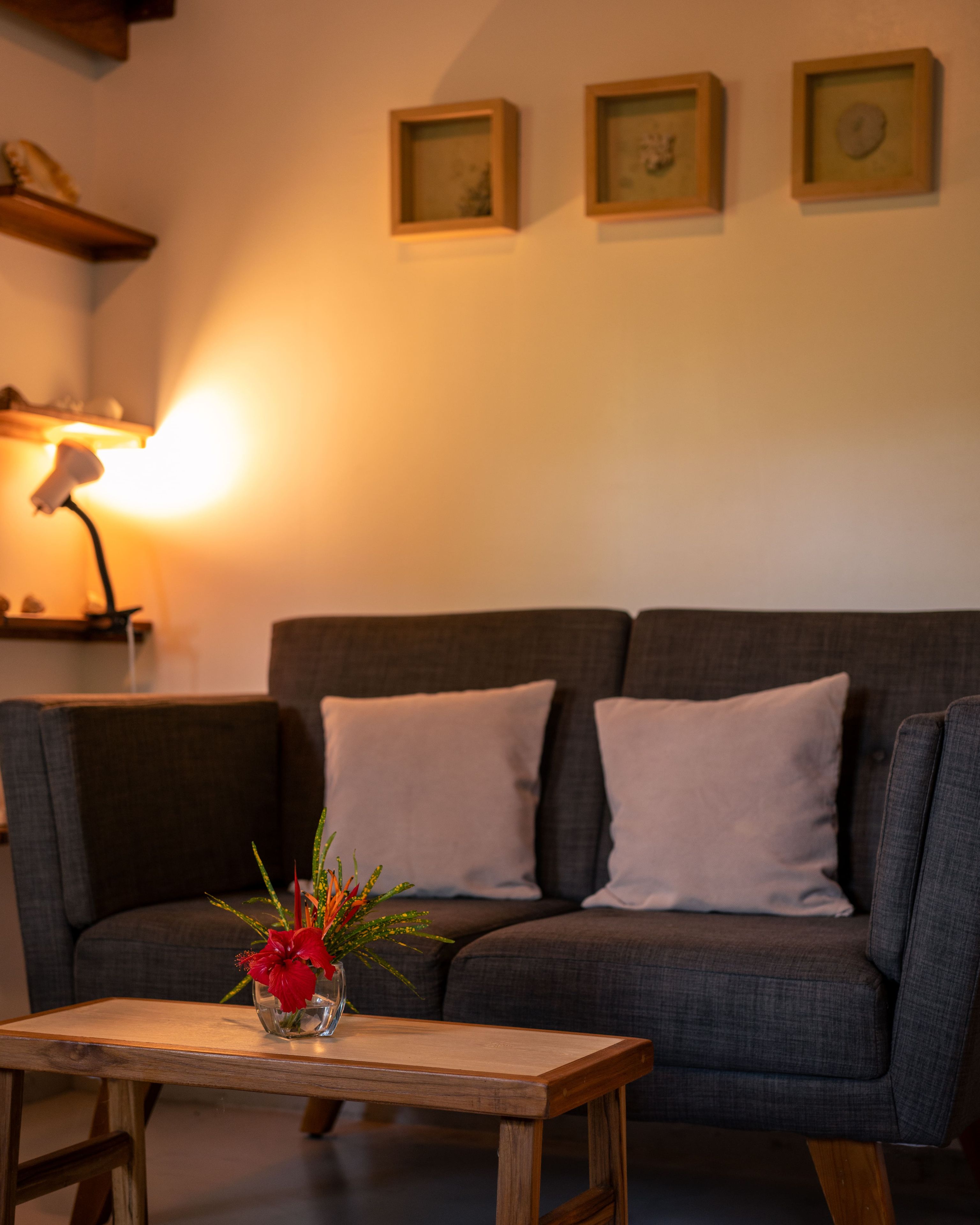 A living room with a sofa, a small wooden table with a vase of flowers, and wall-mounted picture frames.