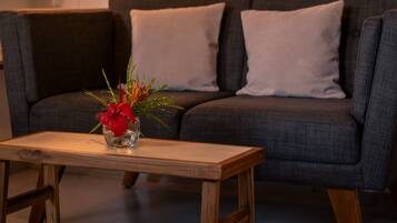 A living room with a sofa, a small wooden table with a vase of flowers, and wall-mounted picture frames.